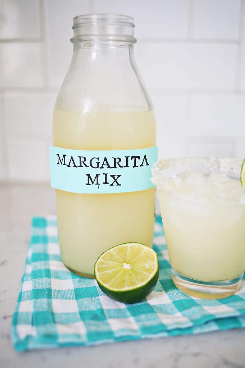 Margarita mix in a jar with a glass of margarita and a lime next to it